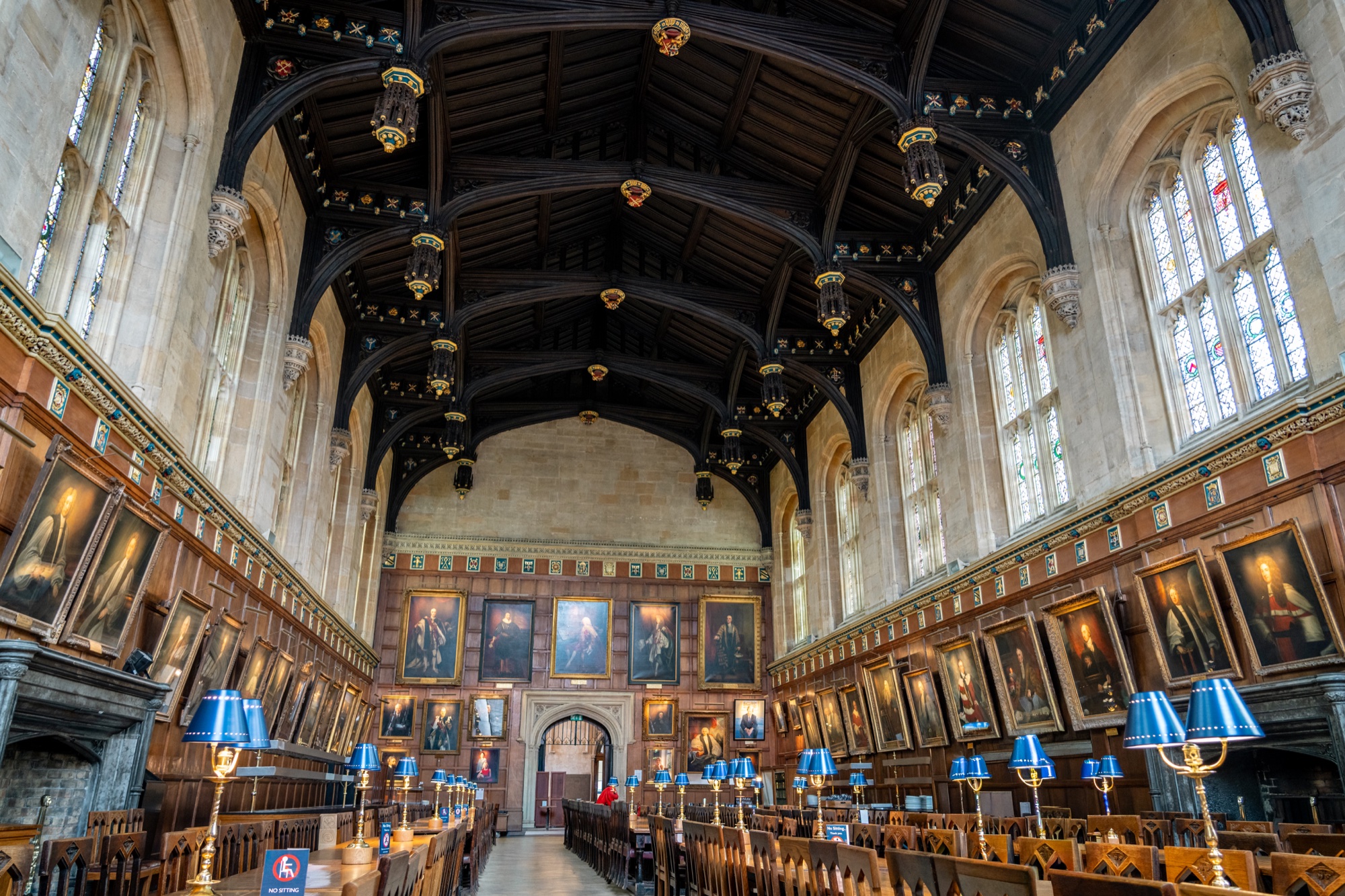 Grand Oxford dining hall with a dark timber ceiling, portrait-lined walls, and blue table lamps