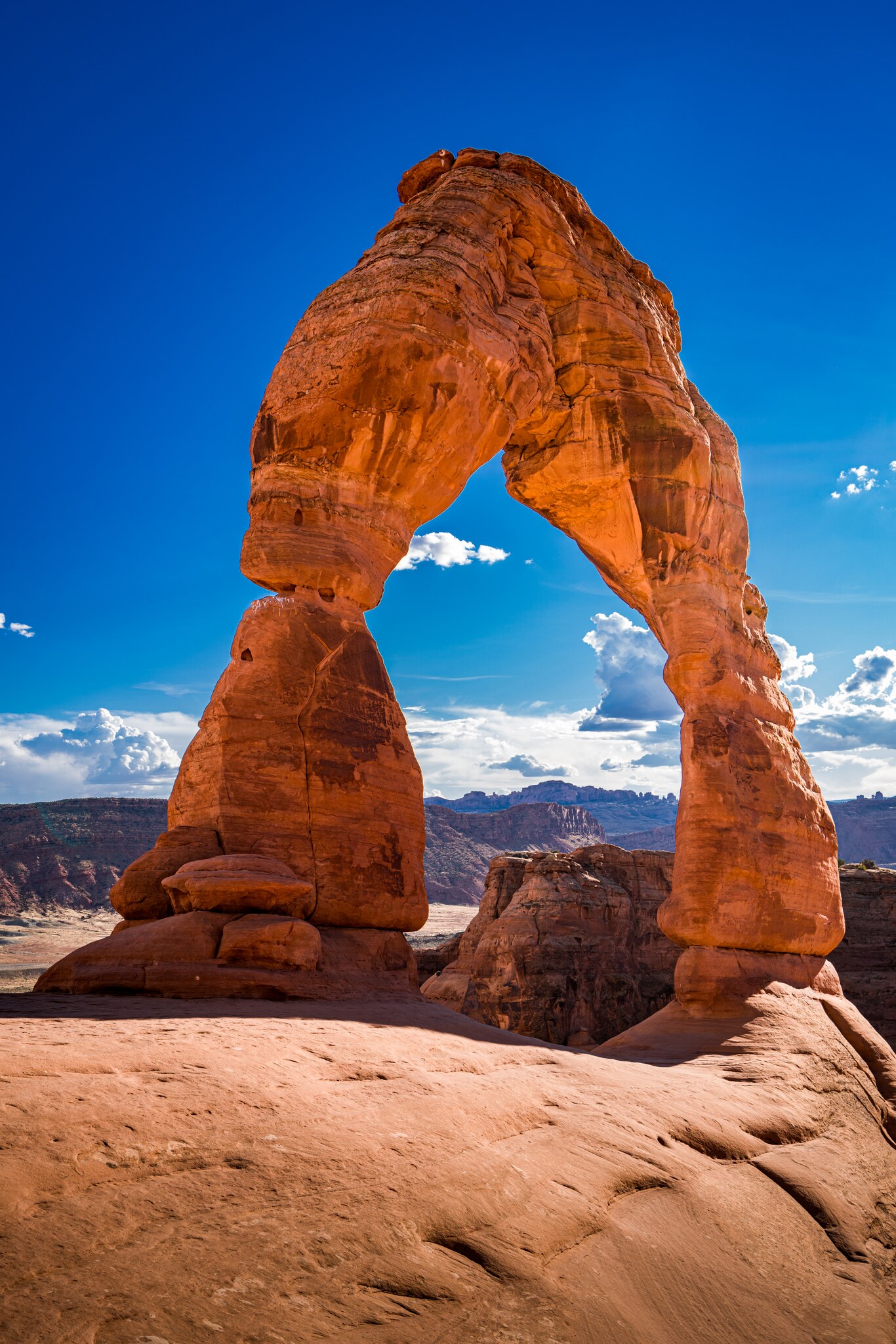 Delicate Arch glowing orange above layered Utah mesas beneath a saturated blue evening sky