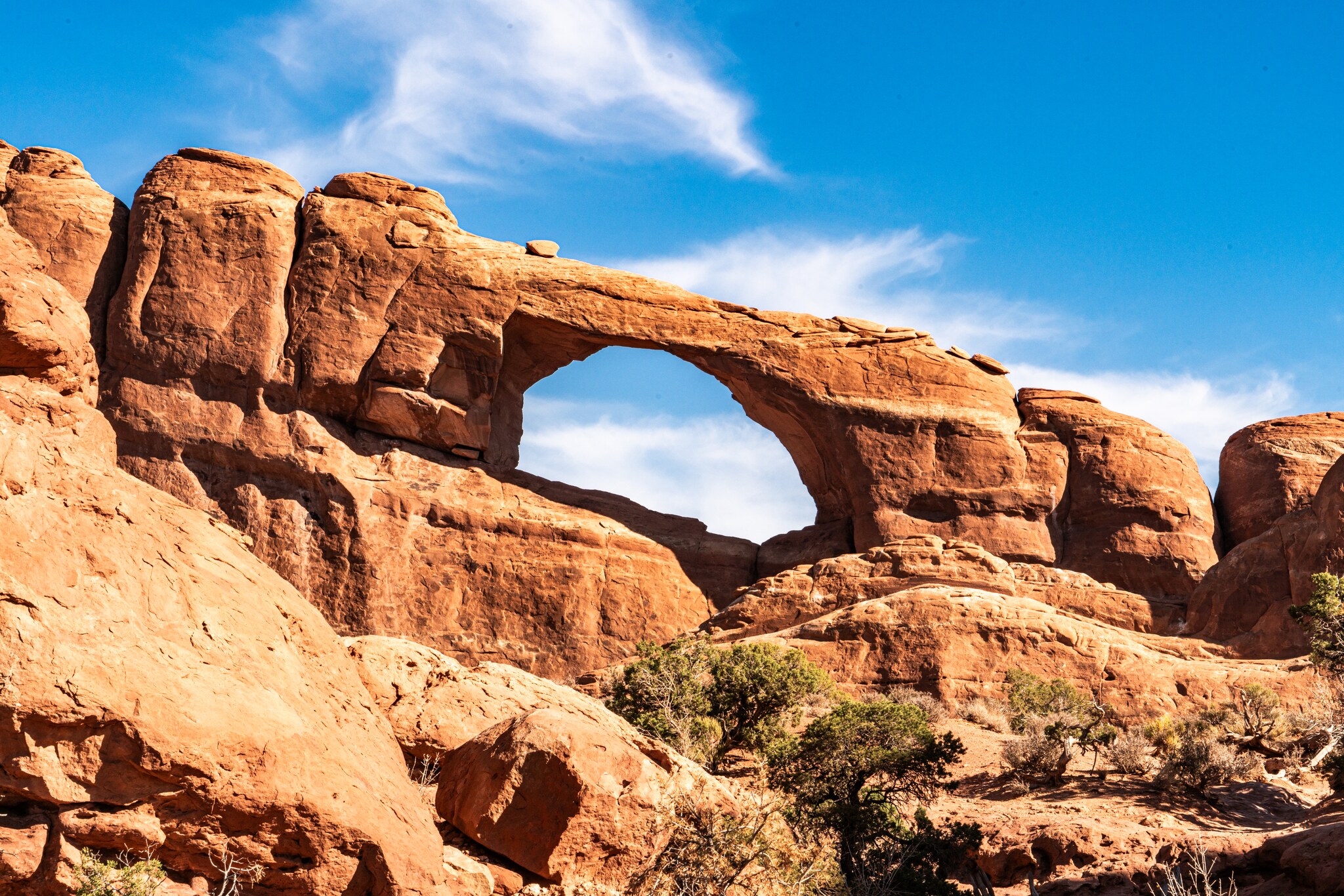 Skyline Arch opening through a long warm sandstone wall beneath thin white clouds